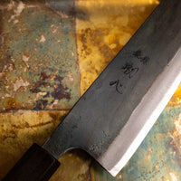 Close-up of the Kurouchi finish on the Kokugei Gyuto Aogami #1 Kuro-uchi Ebony 210mm, highlighting the rustic black surface texture and handcrafted aesthetic.