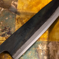 Close-up of the Kokugei Gyuto Aogami #1 Kuro-uchi Ebony 240mm, highlighting the rustic black kurouchi finish, showcasing its hand-forged texture and traditional Japanese craftsmanship.