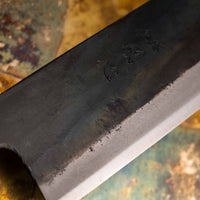Close-up of the Kokugei Gyuto Aogami #1 Kuro-uchi Ebony 240mm, highlighting the rustic black kurouchi finish, showcasing its hand-forged texture and traditional Japanese craftsmanship.