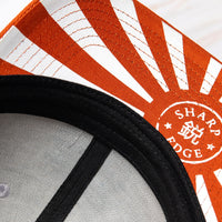 SharpEdge exclusive merch: SharpEdge x Vincent Trinidad Trucker Hat Exclusive SharpEdge design of a brown sumo-fighting bear, armed with our ZDP-189 Bunka Black Japanese knife in collaboration with artist Vincent Trinidad. The bottom of the sturdy visor features the SharpEdge logo within a Japanese rising sun.