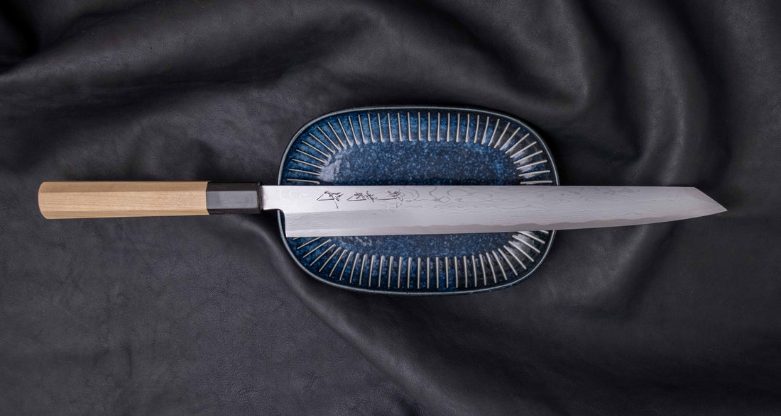 Kawamura Kiritsuke Yanagi Shirogami #1 300mm (11.8") originates from one of the most famous knifemaking centers in Japan, where it was handcrafted by master blacksmiths of the Sakai Kikumori smithy. It represents the pinnacle of Japanese knifemaking. The single-bevel blade is adorned by a stunning damascus pattern.