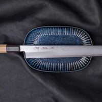 Kawamura Kiritsuke Yanagi Shirogami #1 300mm (11.8") originates from one of the most famous knifemaking centers in Japan, where it was handcrafted by master blacksmiths of the Sakai Kikumori smithy. It represents the pinnacle of Japanese knifemaking. The single-bevel blade is adorned by a stunning damascus pattern.