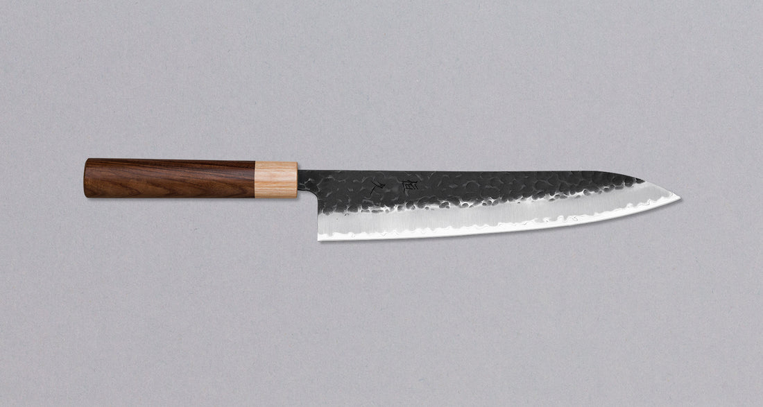 Morado Gyuto Kuro-uchi is a knife with a multipurpose Kuro-uchi protective patina and hammer dents. The centerpiece of this knife is Hitachi's Aogami Super, which is the very top quality of traditional Japanese steels. The Kuro-uchi (black) patina on the upper part of the knife gives it a unique and rustic appearance. 