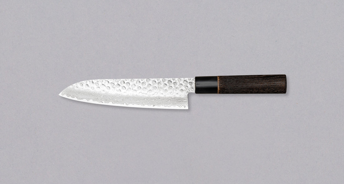 Kawamura Santoku Damascus is a multi-purpose Japanese kitchen knife. The core is made out of stainless AUS-10 steel, wrapped in layers of Damascus steel and the top part of the blade is adorned with hammer prints. The traditional Japanese handle is made out of burnt chestnut wood with a buffalo horn ferrule.