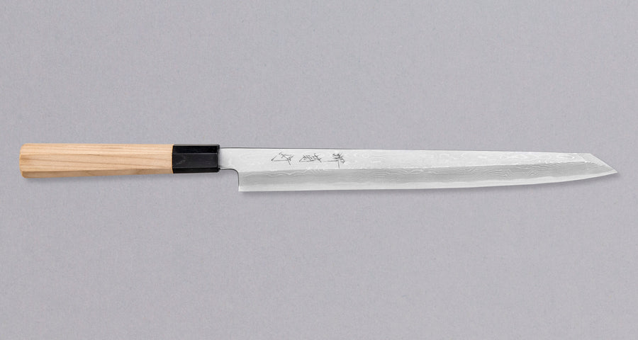 Kawamura Kiritsuke Yanagi Shirogami #1 300mm (11.8") originates from one of the most famous knifemaking centers in Japan, where it was handcrafted by master blacksmiths of the Sakai Kikumori smithy. It represents the pinnacle of Japanese knifemaking. The single-bevel blade is adorned by a stunning damascus pattern.