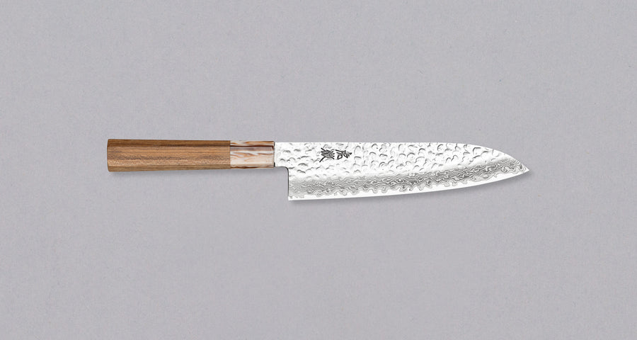 The Kotetsu Santoku VG-10 Damascus 180mm (7.08") is a large multi-purpose Janapese knife with visible hammer prints, a damascus pattern and a classic Japanese (wa-style) teak handle. It will impress anyone who appreciates aesthetically designed kitchen utensils.
