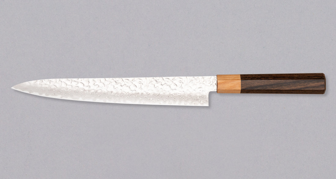 The Kotetsu Sujihiki VG-10 Damascus 240mm (9.5") is a long and narrow Japanese slicer with visible hammer prints, a damascus pattern, and a classic Japanese (wa-style) pakka wood handle. It will impress anyone who appreciates aesthetically designed kitchen utensils.