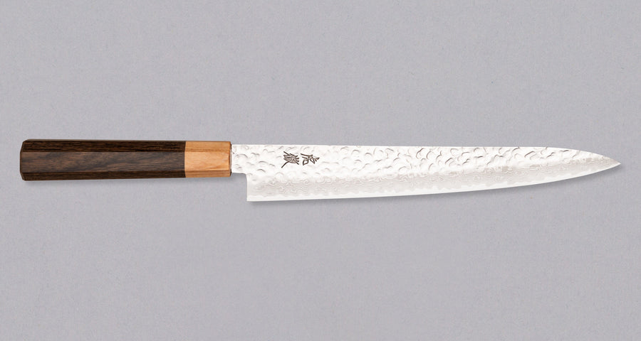 The Kotetsu Sujihiki VG-10 Damascus 240mm (9.5") is a long and narrow Japanese slicer with visible hammer prints, a damascus pattern, and a classic Japanese (wa-style) pakka wood handle. It will impress anyone who appreciates aesthetically designed kitchen utensils.