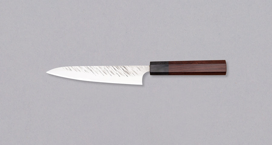 Kurosaki Petty Fujin is a uniquely looking blade from the talented Yu Kurosaki. Petty is a small kitchen knife perfect for all those delicate tasks where a larger knife is deemed unwieldy. Core from SG2 powder steel is enveloped in softer steel with a striking tsuchime pattern. Fitted with an octagonal rosewood handle.