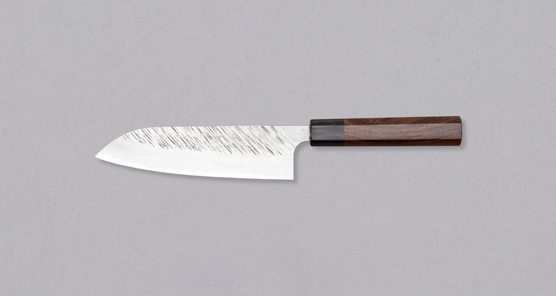 Kurosaki Santoku Fujin is another uniquely looking blade from the hands of the talented young master blacksmith Yu Kurosaki. Made from SG2 powder steel, the blade is adorned with a unique tsuchime pattern and fitted with a rosewood handle. Optimal for everyday, versatile use, whether you are a home cook or a pro chef.