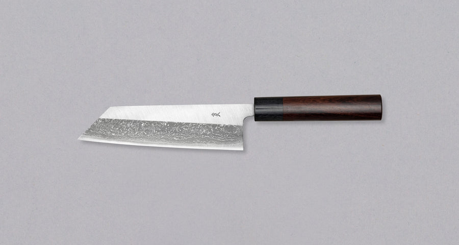 Muneishi Bunka Aogami #2 Damascus 165mm is a multi-purpose Japanese kitchen knife, suitable for preparing meat, fish and vegetables, with a special "K-tip" for precise cuts. The minimalistic polished blade finish shifts into a misty damascus pattern, giving the knife an elegant, dreamy look. Fitted with rosewood handle.