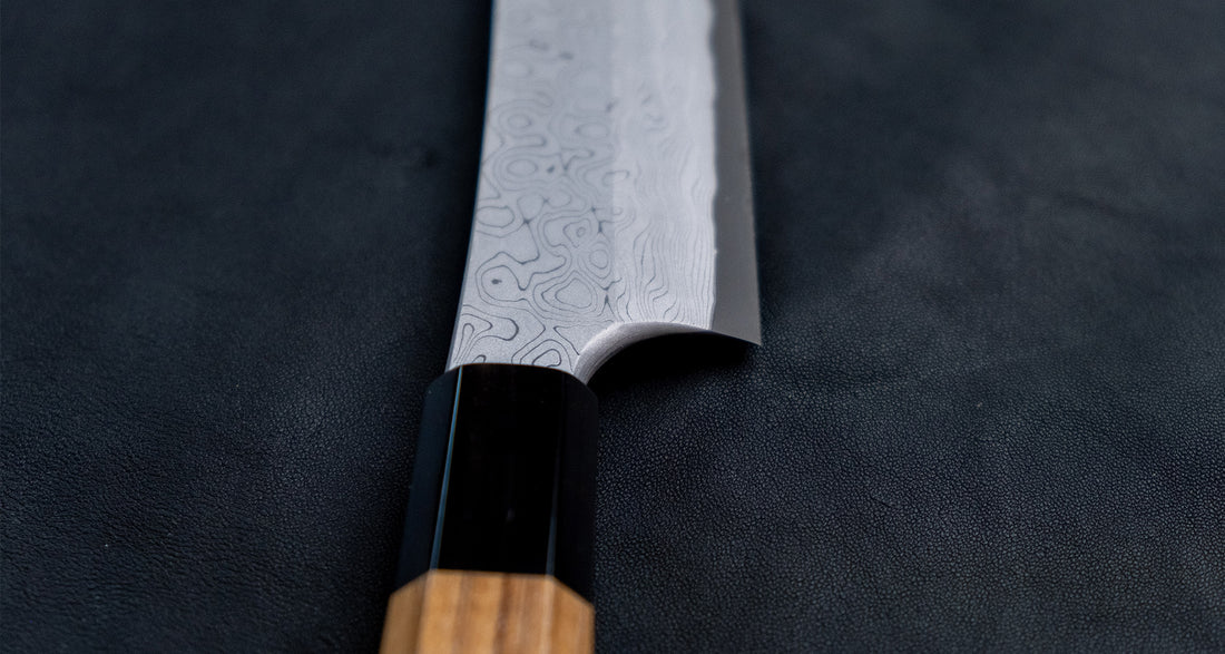The quality and craftsmanship of this Nigara Kurozome Yanagiba Aogami #2 Damascus 270mm (10.6") is simply superb - from the beautifully polished choil to the unique damascus pattern that surrounds the spine of the blade and extends to its back. The outer layers of the blade have a pearl mosaic-like appearance, which you won't find often even in the most high-end blades.