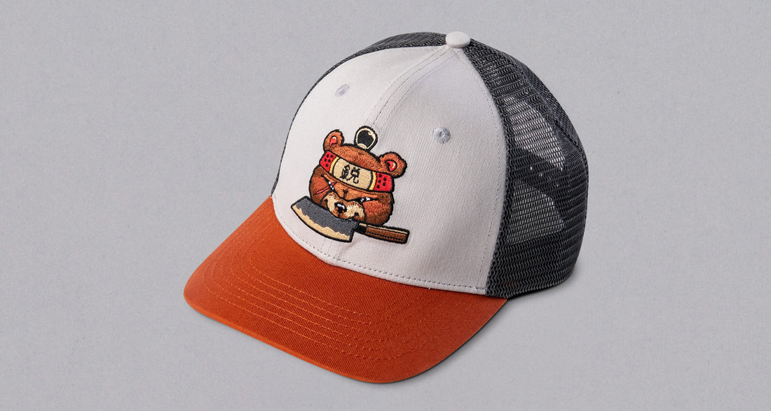 SharpEdge exclusive merch: SharpEdge x Vincent Trinidad Trucker Hat Exclusive SharpEdge design of a brown sumo-fighting bear, armed with our ZDP-189 Bunka Black Japanese knife in collaboration with artist Vincent Trinidad. The bottom of the sturdy visor features the SharpEdge logo within a Japanese rising sun.