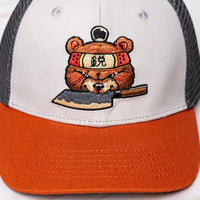 SharpEdge exclusive merch: SharpEdge x Vincent Trinidad Trucker Hat Exclusive SharpEdge design of a brown sumo-fighting bear, armed with our ZDP-189 Bunka Black Japanese knife in collaboration with artist Vincent Trinidad. The bottom of the sturdy visor features the SharpEdge logo within a Japanese rising sun.