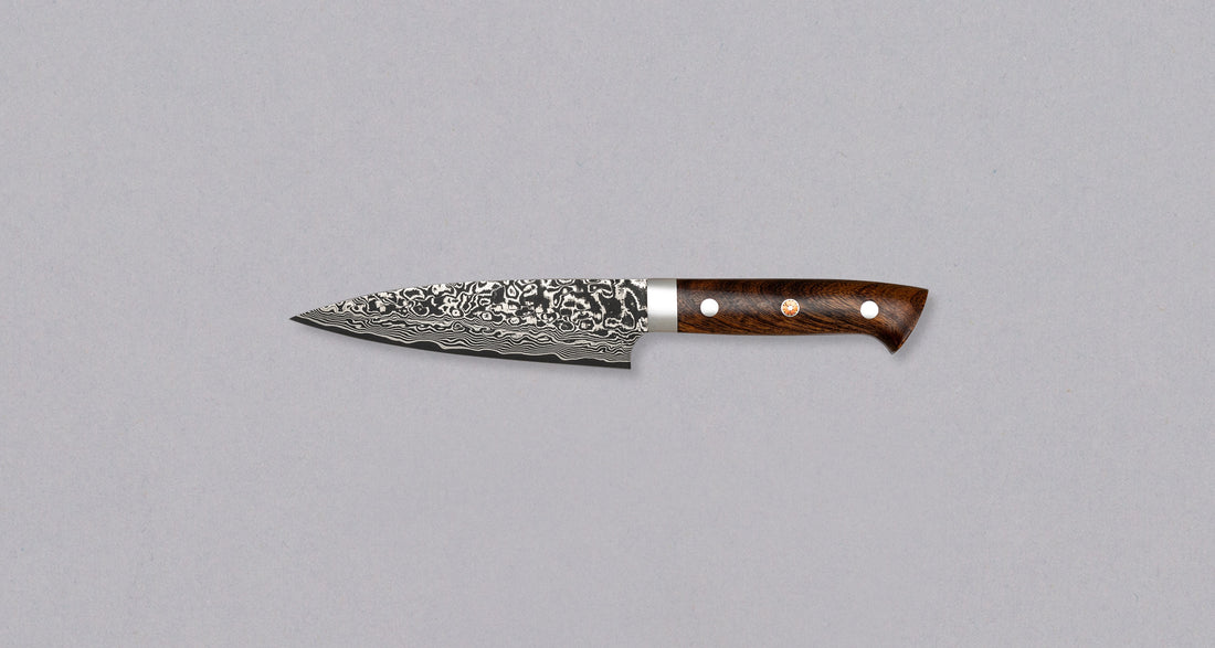 Saji Petty R2 Ironwood 130mm is not just a looker. The core is made of powder R2/SG2 steel, tempered to around 63 HRC, and clad into layers of rust-resistant stainless steel which creates a unique damascus pattern. The knife is stored in a traditional Japanese wooden box with burned Saji trademark kanji on top.