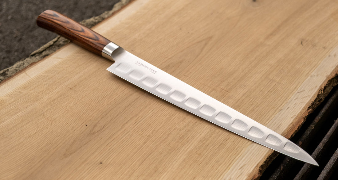 Tamahagane San Sujihiki (or slicer) knife is primarily intended for long pulls and precise cuts of meat and fish. Dimples on the blade also have a practical function: the air in the clefts acts as an anti-stick coating between the knife and the food and reduces the drag during cutting.