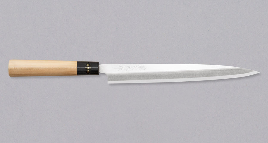Pictured: Japanese knife Tojiro Yanagiba from the front. Tojiro Yanagiba 240mm (9.4") is a handy low-maintenance single-bevel knife suitable for preparing meat and fish. With a core of Shirogami #1 steel and ni-mai lamination, it is easy to resharpen and keep sharp long-term. It features a D-shaped magnolia handle with a water buffalo horn ferrule, and a migaki blade finish.