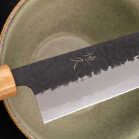 Tsunehisa Kiritsuke AS Kuro-uchi 240mm (9.4") is a multi-purpose knife with a black Kuro-uchi protective patina and tsuchime hammer indentations. Its length makes it great for cutting larger pieces of meat and fish. The Kuro-uchi (black) patina on the upper part of the knife gives it a unique and rustic appearance.