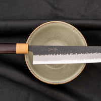 Tsunehisa Kiritsuke AS Kuro-uchi 240mm (9.4") is a multi-purpose knife with a black Kuro-uchi protective patina and tsuchime hammer indentations. Its length makes it great for cutting larger pieces of meat and fish. The Kuro-uchi (black) patina on the upper part of the knife gives it a unique and rustic appearance.