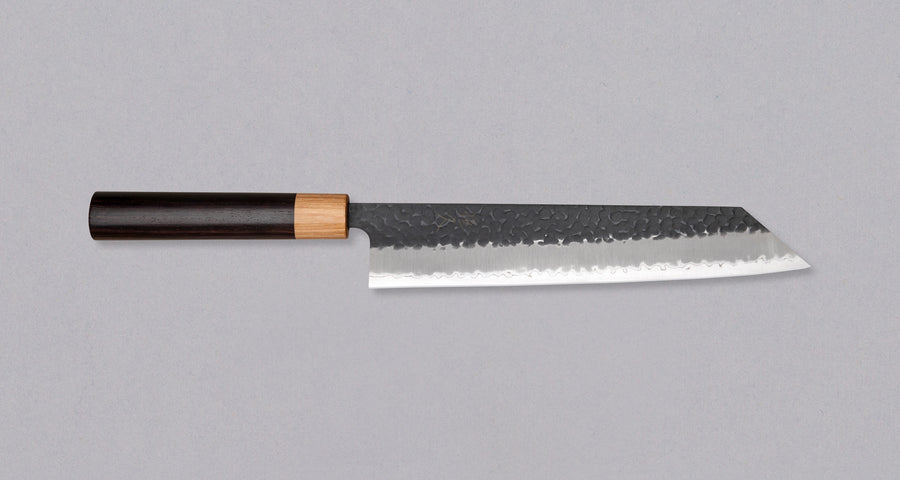 Tsunehisa Kiritsuke AS Kuro-uchi 240mm (9.4") is a multi-purpose knife with a black Kuro-uchi protective patina and tsuchime hammer indentations. Its length makes it great for cutting larger pieces of meat and fish. The Kuro-uchi (black) patina on the upper part of the knife gives it a unique and rustic appearance.