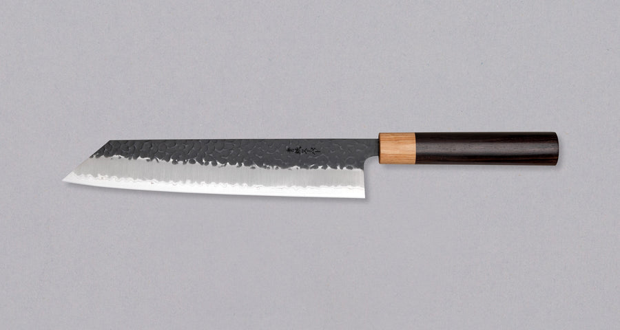 Tsunehisa Kiritsuke AS Kuro-uchi 240mm (9.4") is a multi-purpose knife with a black Kuro-uchi protective patina and tsuchime hammer indentations. Its length makes it great for cutting larger pieces of meat and fish. The Kuro-uchi (black) patina on the upper part of the knife gives it a unique and rustic appearance.