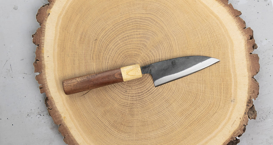 This Ajikiri SUJ-2 blade made by Yoshida Hamono is a Japanese knife for small fish. It's fitted with an oval rosewood handle which is topped with a cedar ferrule. The blade is forged from SUJ-2 steel with a hardness is 63-64 HRC, which holds its edge for a long time and is very easy to resharpen.