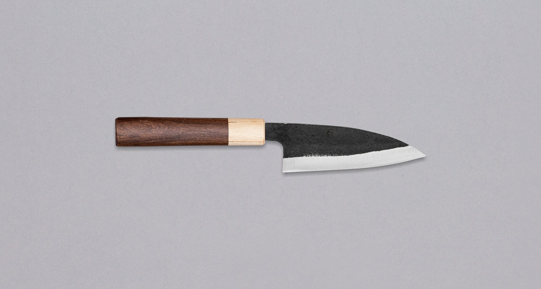 This Ajikiri SUJ-2 blade made by Yoshida Hamono is a Japanese knife for small fish. It's fitted with an oval rosewood handle which is topped with a cedar ferrule. The blade is forged from SUJ-2 steel with a hardness is 63-64 HRC, which holds its edge for a long time and is very easy to resharpen.