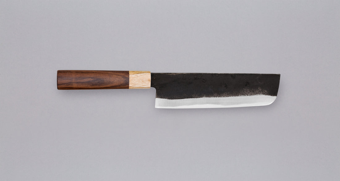 This Nakiri Kyusyu SUJ-2 blade is fitted with an oval rosewood handle, topped with a cedar ferrule. A traditional Japanese knife for cutting vegetables. The blade is forged from SUJ-2 steel with a hardness is 63-64 HRC, which holds its edge for a long time and is very easy to resharpen.