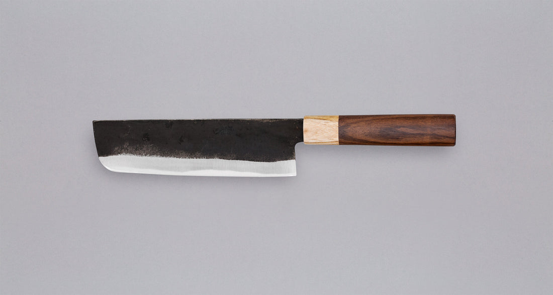 This Nakiri Kyusyu SUJ-2 blade is fitted with an oval rosewood handle, topped with a cedar ferrule. A traditional Japanese knife for cutting vegetables. The blade is forged from SUJ-2 steel with a hardness is 63-64 HRC, which holds its edge for a long time and is very easy to resharpen.